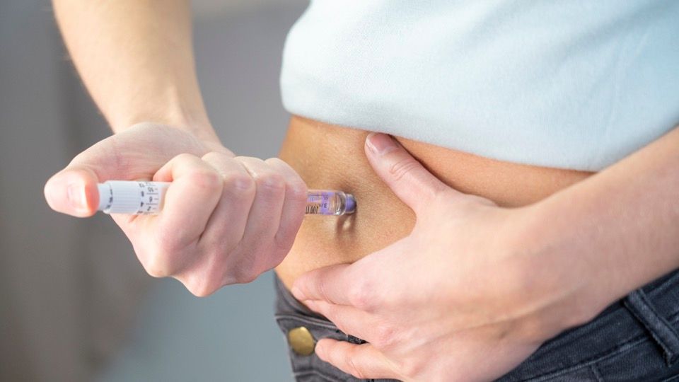 A person injecting a syringe into pinched skin on the abdomen