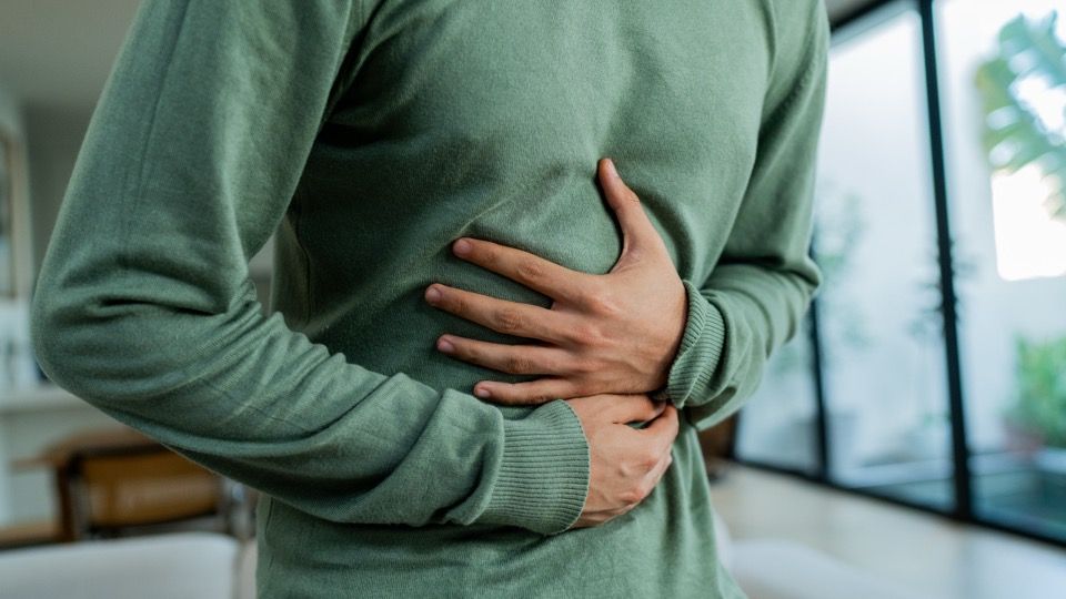 A person in a green sweater holding their abdomen with both hands