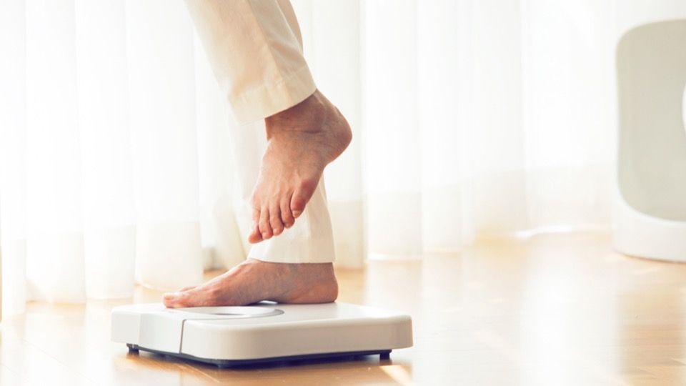 Mounjaro and lean mass - bare foot stepping onto a bathroom scale on a wooden floor