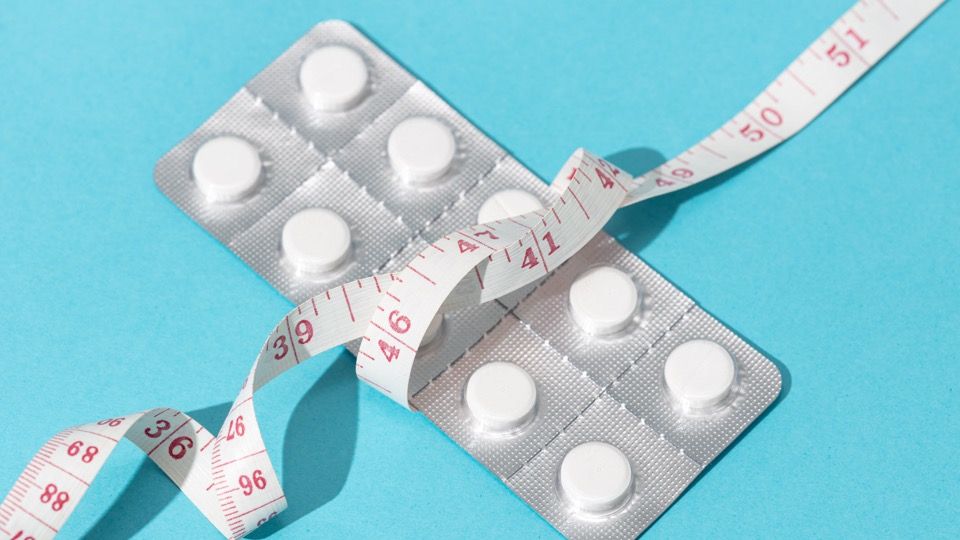 Blister packs of white tablets with a tape measure wrapped around them on a blue background