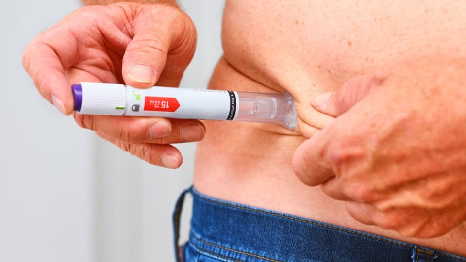 A hand injecting a 15 mg single-dose pen into pinched skin on the abdomen