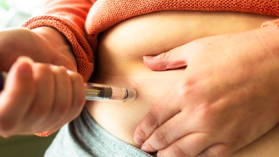 Close-up of a syringe being injected into pinched skin on the abdomen