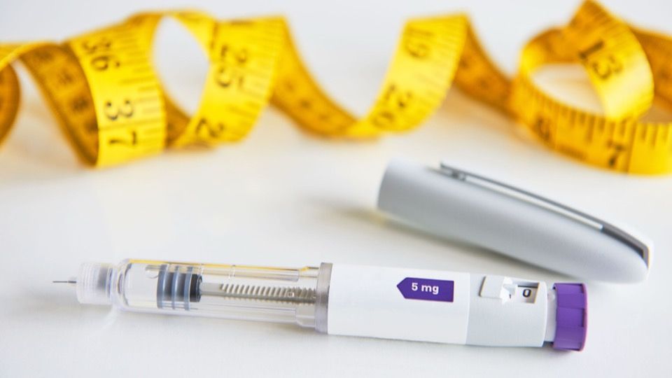 Mounjaro prefilled pen with a purple dose knob beside a yellow tape measure on a white background