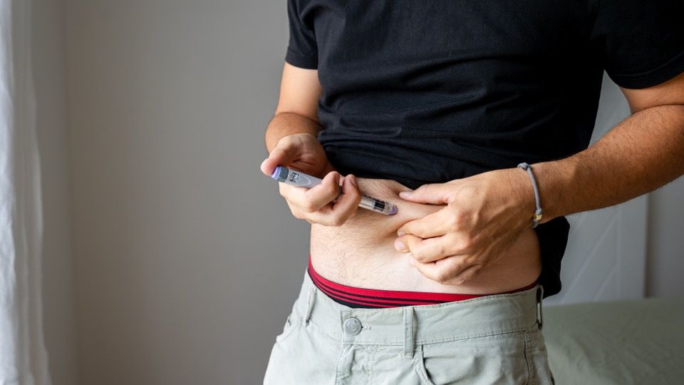 A man injecting an injection pen into pinched skin on the abdomen