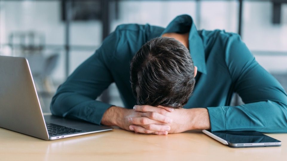 Mounjaro and drowsiness - man resting his head on his folded arms at an office desk