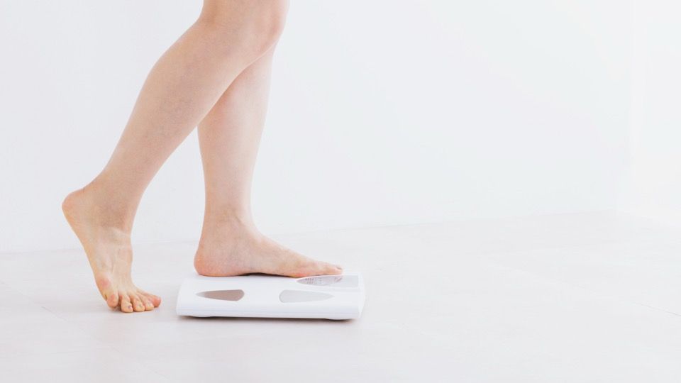 Bare feet stepping onto a white bathroom scale