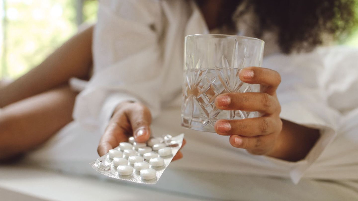 person holding allergy medicine tablet and water glass at home