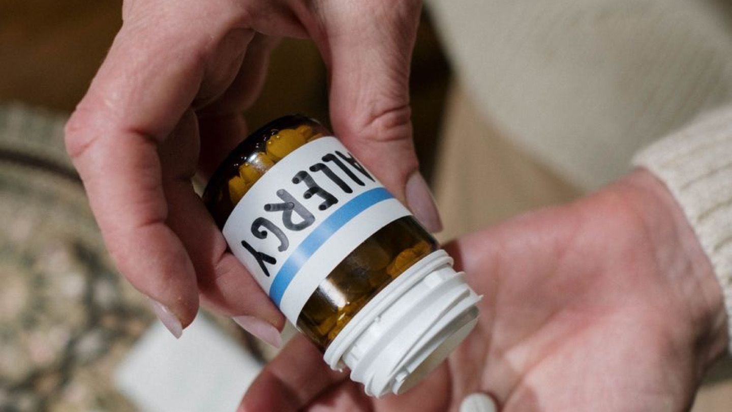 person holding allergy medicine tablet and water glass at home