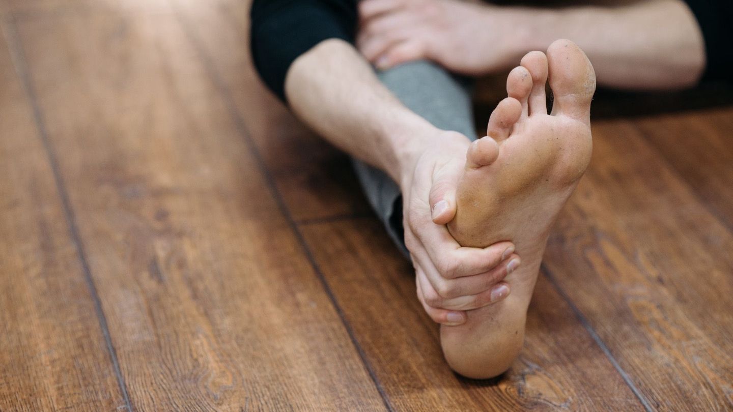바닥에 앉아 발목을 당기며 발바닥 스트레칭을 하는 사람의 다리